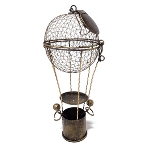 May include: A gold metal hot air balloon shaped decorative object with a wire mesh basket and a round top. The balloon has a small, round, metal lid on top.
