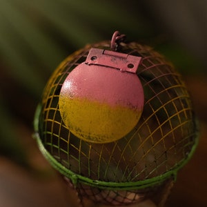 May include: A pink and yellow metal hot air balloon with a wire cage. The balloon has a hinge and is decorated with a green and yellow striped pattern.