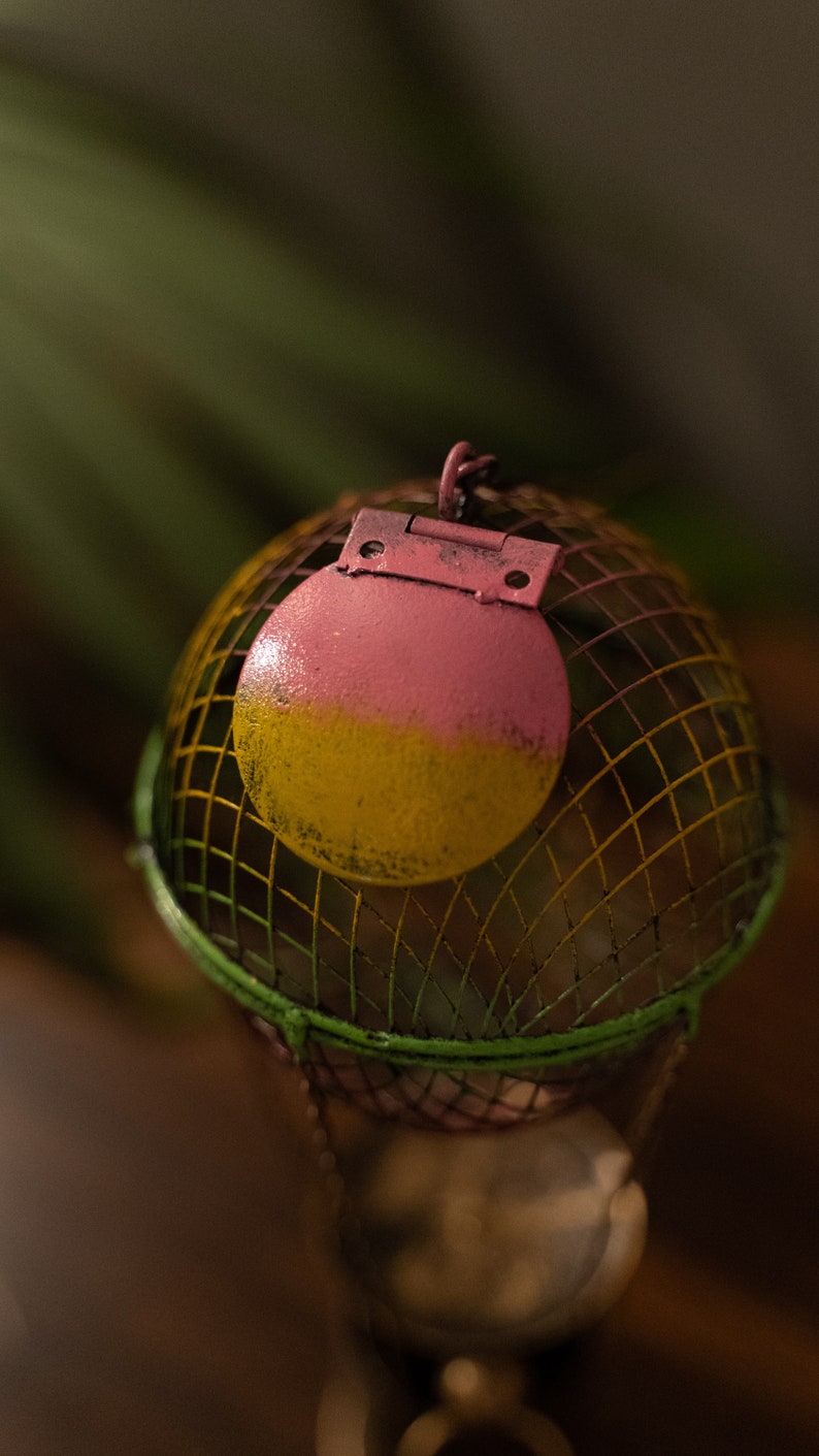 May include: A pink and yellow metal hot air balloon with a wire cage. The balloon has a hinge and is decorated with a green and yellow striped pattern.