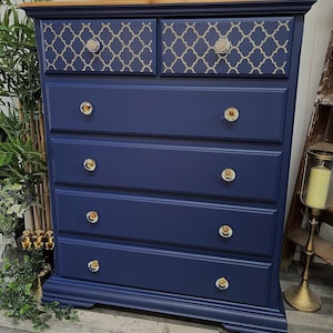 May include: A navy blue chest of drawers with six drawers and gold-toned crystal knobs. The top two drawers have a decorative pattern in gold and beige.