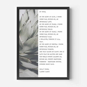 Op de afbeelding: Een zwart ingelijst print met een citaat van Albert Camus over het vinden van innerlijke kracht. Het citaat is gedrukt op een witte achtergrond en toont een foto van een groene succulent.