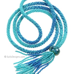 May include: A long, beaded necklace with a turquoise and blue ombre effect. The necklace has a tassel at the end and a large, round, green glass bead.