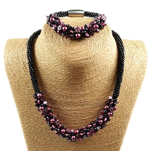 May include: A black beaded necklace and matching bracelet set. The necklace and bracelet feature clusters of dark pink beads and a magnetic clasp. The jewelry is displayed on a tan bust form.