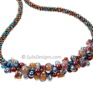 May include: A multi-strand necklace featuring a cluster of colourful beads in shades of blue, brown, and pink. The beads are arranged in a cascading pattern, creating a unique and eye-catching design.