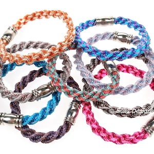 May include: A set of eight colourful braided rope bracelets with silver magnetic clasps. The bracelets are in various colours, including pink, blue, purple, and orange.