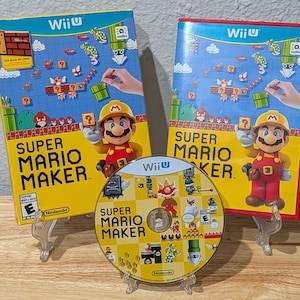 Puede incluir: Dos cajas de juego para Wii U y un disco de Super Mario Maker. Las cajas amarilla y roja muestran a Mario con ropa de construcción, gráficos de niveles y el logo de Wii U. El disco circular presenta varios personajes e iconos del juego.