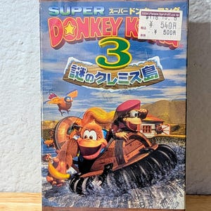 Könnte beinhalten: Eine Vintage Super Nintendo Donkey Kong 3 Videospiel-Cartridge-Box. Die Box zeigt farbenfrohe Kunstwerke von Donkey Kong und anderen Charakteren in einer tropischen Umgebung. Der Spieletitel und das Nintendo-Logo sind deutlich sichtbar.