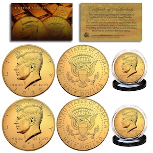 May include: Two gold-plated 2022 half dollar coins featuring John F. Kennedy on one side and the United States seal on the other. The coins are displayed in clear plastic capsules with black bases.
