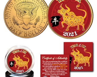 May include: A gold-coloured coin with the inscription "United States of America Half Dollar" on one side and a red and gold image of an ox with the inscription "Year of the Ox 2021" on the other side. The coin is displayed in a clear plastic case with a black base.