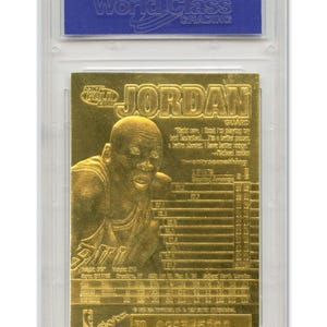 May include: A gold-colored Michael Jordan basketball card encased in a protective plastic holder. The card features an image of Jordan and the name "JORDAN" in large letters. The card also includes statistics and the text "www.worldclassgrading.com".