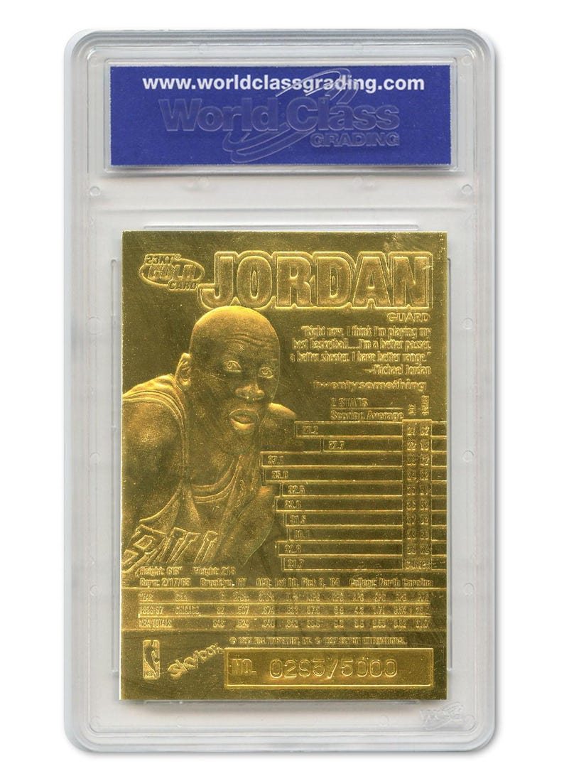 May include: A gold-colored Michael Jordan basketball card encased in a protective plastic holder. The card features an image of Jordan and the name "JORDAN" in large letters. The card also includes statistics and the text "www.worldclassgrading.com".
