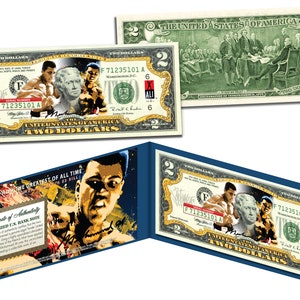 May include: A colorized $2 bill featuring a portrait of Muhammad Ali, the greatest of all time, with a black and yellow background. The bill is framed in a blue and gold border. The back of the bill features a scene of the signing of the Declaration of Independence.