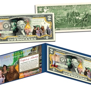 May include: A two dollar bill featuring a colorized image of the Wizard of Oz characters, including Dorothy, the Scarecrow, the Tin Man, and the Cowardly Lion. The bill is framed with a blue border and includes a certificate of authenticity.