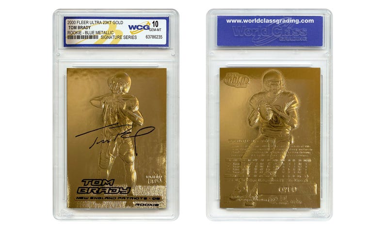 Puede incluir: Dos tarjetas de novato de Tom Brady doradas en estuches protectores. Las tarjetas presentan una imagen en relieve de Brady con uniforme de f&uacute;tbol. Una tarjeta tiene una firma. Los estuches tienen etiquetas con texto, incluyendo "2000 Fleer Ultra 23KT Gold" y "Signature Series".