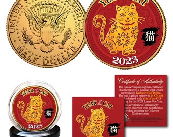 May include: A gold-coloured coin featuring a red and gold design of a cat. The coin is displayed in a clear plastic case with a black base. The coin is surrounded by a red circle with the text "Year of the Cat" and "2023" in gold lettering. The coin also has the text "猫" in gold lettering. This commemorative coin celebrates the Chinese New Year of the Cat.
