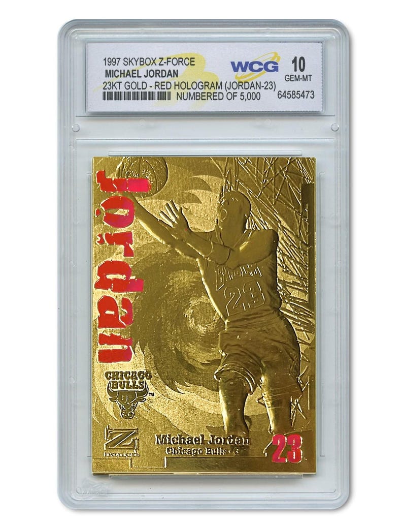 May include: A gold-colored Michael Jordan trading card from the 1997 Skybox Z-Force series. The card features a red hologram of Jordan in action, with the Chicago Bulls logo and the number 23. The card is graded WCG 10.