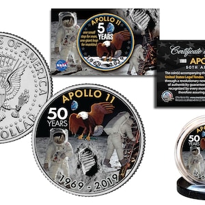 May include: A silver half dollar coin with the inscription "United States of America" and "Half Dollar" on the obverse side. The reverse side features a colour image of the Apollo 11 mission with the text "Apollo 11 50 Years 1969-2019".