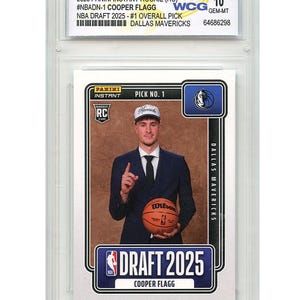 May include: A 2025 Panini Instant Rookie card of Cooper Flagg, #1 overall pick for the Dallas Mavericks. The card is graded WCG 10 GEM-MT and shows Flagg in a suit holding a basketball. The card is encased in a protective holder.