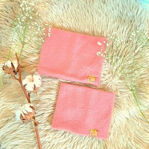 May include: Two pink fleece wrist warmers with a small gold tag that says "Iro" on each. The warmers are on a fluffy white surface.