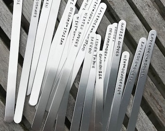 May include: A set of metal plant markers with various herb and flower names engraved on them, including Lavender, Rosemary, Sage, Chives, Thyme, Mint, and Oregano.