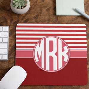 May include: Red and white striped mouse pad with a pink circle monogrammed with the letters "MRK" in white.