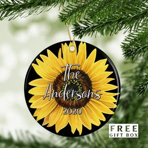 May include: A round ceramic ornament with a black background and a yellow sunflower. The sunflower has a brown center and the text "The Andersons 2020" is printed on the sunflower.