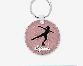 May include: A pink round keychain with a silhouette of a figure ice skating and the name "Alissa" in a retro font.