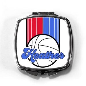 May include: A white compact mirror with a silver trim. The mirror features a basketball with red and blue stripes and the name "Heather" in blue cursive.