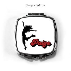 May include: A silver compact mirror with a white background. The image features a silhouette of a person dancing with the name "Paige" in red letters.