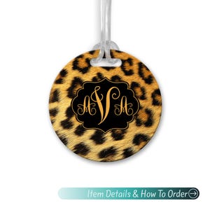 May include: Round luggage tag with a leopard print background and a black and gold monogram in the center. The monogram is "AVA".