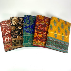 May include: Five fabric-covered journals with different floral patterns. The journals are arranged in a row from left to right, with the colors ranging from light to dark. The journals are all closed and have a simple design.