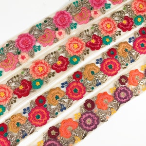 May include: Multicolored floral embroidered trim with gold glitter accents on a sheer white fabric. The trim is layered to show the different colors and designs.