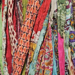 May include: Close-up of a collection of colorful fabric strips. The strips feature various patterns and colors, including red, orange, green, blue, and pink. The fabrics appear to be made of silk or a similar material, with a flowing, draped appearance.