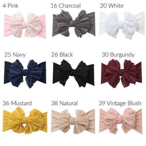 May include: A collection of nine fabric headbands with large, ruffled bows in various colors labeled 4 Pink, 16 Charcoal, 20 White, 25 Navy, 26 Black, 30 Burgundy, 36 Mustard, 38 Natural, and 39 Vintage Blush, each featuring a textured, layered design.