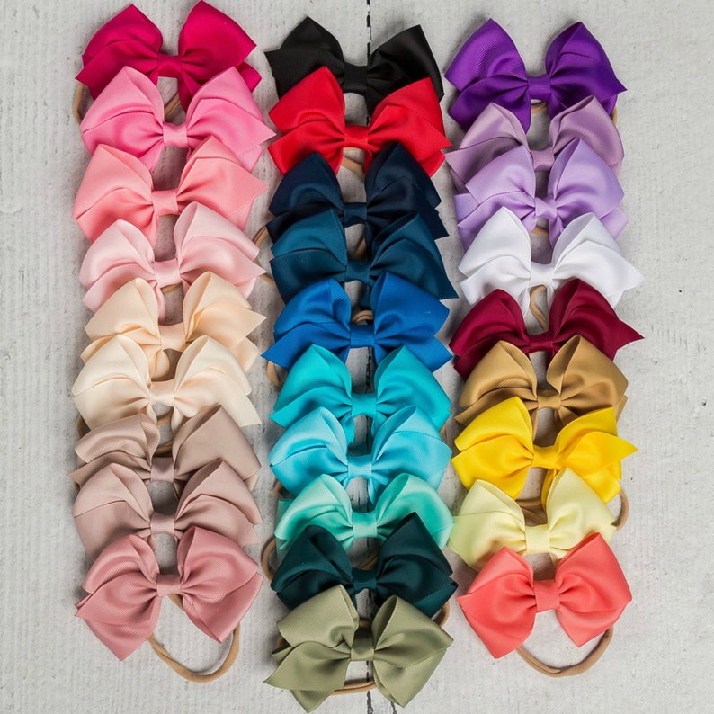 May include: A set of 18 hair bows in various colors, including red, blue, green, yellow, and pink. The bows are made of satin ribbon and are attached to elastic headbands.
