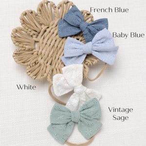 May include: Four different colors of fabric headbands with bows. The colors are white, baby blue, French blue, and vintage sage.