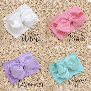 Peut inclure: Quatre bandeaux pour b&eacute;b&eacute; en blanc, rose, lavande et aqua. Chaque bandeau est orn&eacute; d'un grand n&oelig;ud d&eacute;coratif. Les couleurs sont &eacute;tiquet&eacute;es avec du texte en cursive : "White", "Pink", "Lavender" et "Aqua". Les bandeaux sont pr&eacute;sent&eacute;s sur une surface tiss&eacute;e.