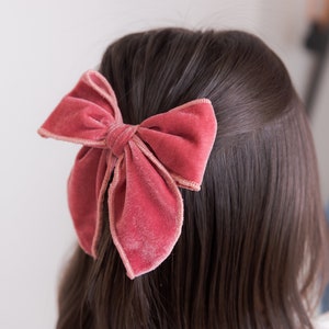 May include: A large, dusty rose velvet bow hair clip. The bow is tied in a classic shape with a center knot.