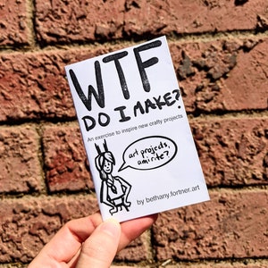 Könnte beinhalten: Ein weißes Heft mit dem Titel "WTF DO I MAKE?" in fetten schwarzen Buchstaben. Das Heft zeigt eine Cartoon-Illustration und den Text "Eine Übung, um neue Bastelprojekte zu inspirieren." Der Name des Künstlers ist ebenfalls enthalten.