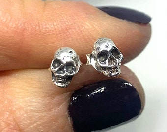 May include: A pair of silver skull stud earrings. The skulls are small and detailed, with a textured finish.