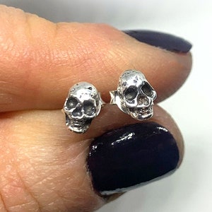 May include: A pair of silver skull stud earrings. The skulls are small and detailed, with a textured finish.