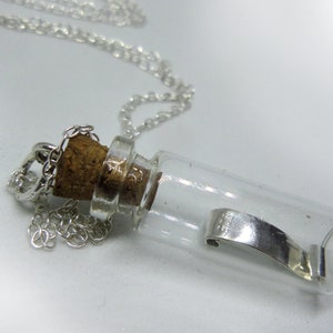May include: A silver chain necklace with a small glass bottle pendant. The bottle has a cork stopper and contains a silver charm.