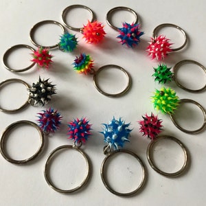 May include: A set of 12 colorful spiky keychains with silver key rings. The keychains are made of rubber and have a variety of colors, including red, blue, green, yellow, and black.