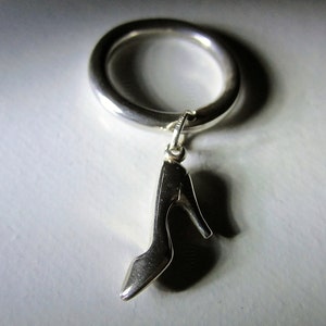 May include: A silver ring with a silver high heel shoe charm hanging from it.