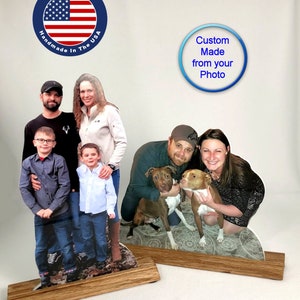 May include: Two custom-made photo sculptures on wooden bases. The first sculpture features a family of four, including two children, standing on a grassy background. The second sculpture features a couple with two brown and white pit bull dogs. Both sculptures have a blue circle with white text that reads "Custom Made from your Photo".