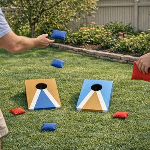 May include: Two wooden cornhole boards with blue and tan paint, and a hole in the top. Several blue and red bean bags are scattered on the grass. Two people are playing cornhole in a garden.
