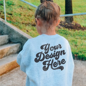 May include: A light blue sweatshirt with the text "Your Design Here" printed on the back in a retro font.