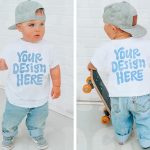 May include: A white t-shirt with the text "Your Design Here" in blue lettering. The shirt is being modeled by a child wearing a gray baseball cap and blue jeans.
