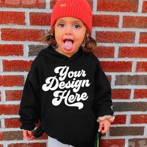 Może przedstawiać: Czarna bluza z kapturem z napisem "Your Design Here" w białym retro-foncie. Małe dziecko nosi bluzę i czerwoną czapkę.