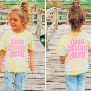May include: A yellow and white tie-dye t-shirt with the text "YOUR DESIGN HERE" in pink. The shirt is being worn by a child.